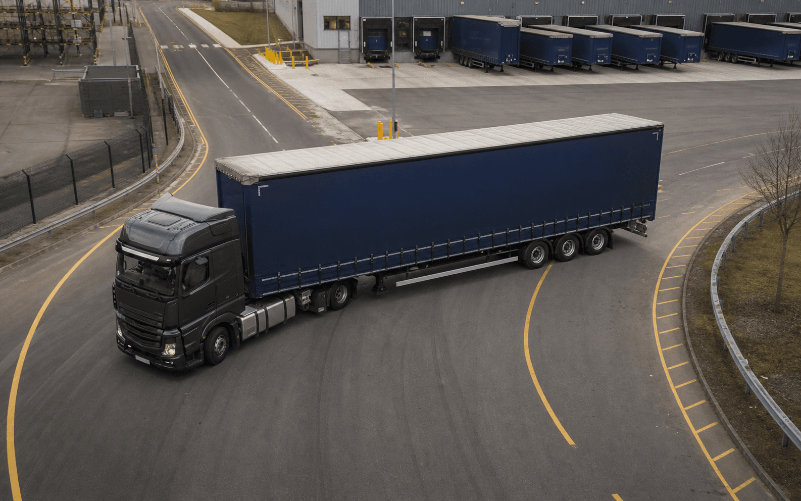 Long articulated lorry following a wide marked turn inside a logistics depot